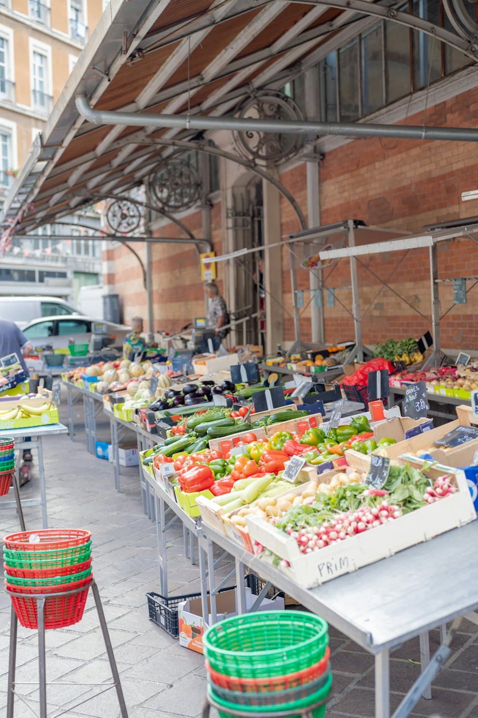 Outdoor market stall with fresh vegetables and fruits under an awning.