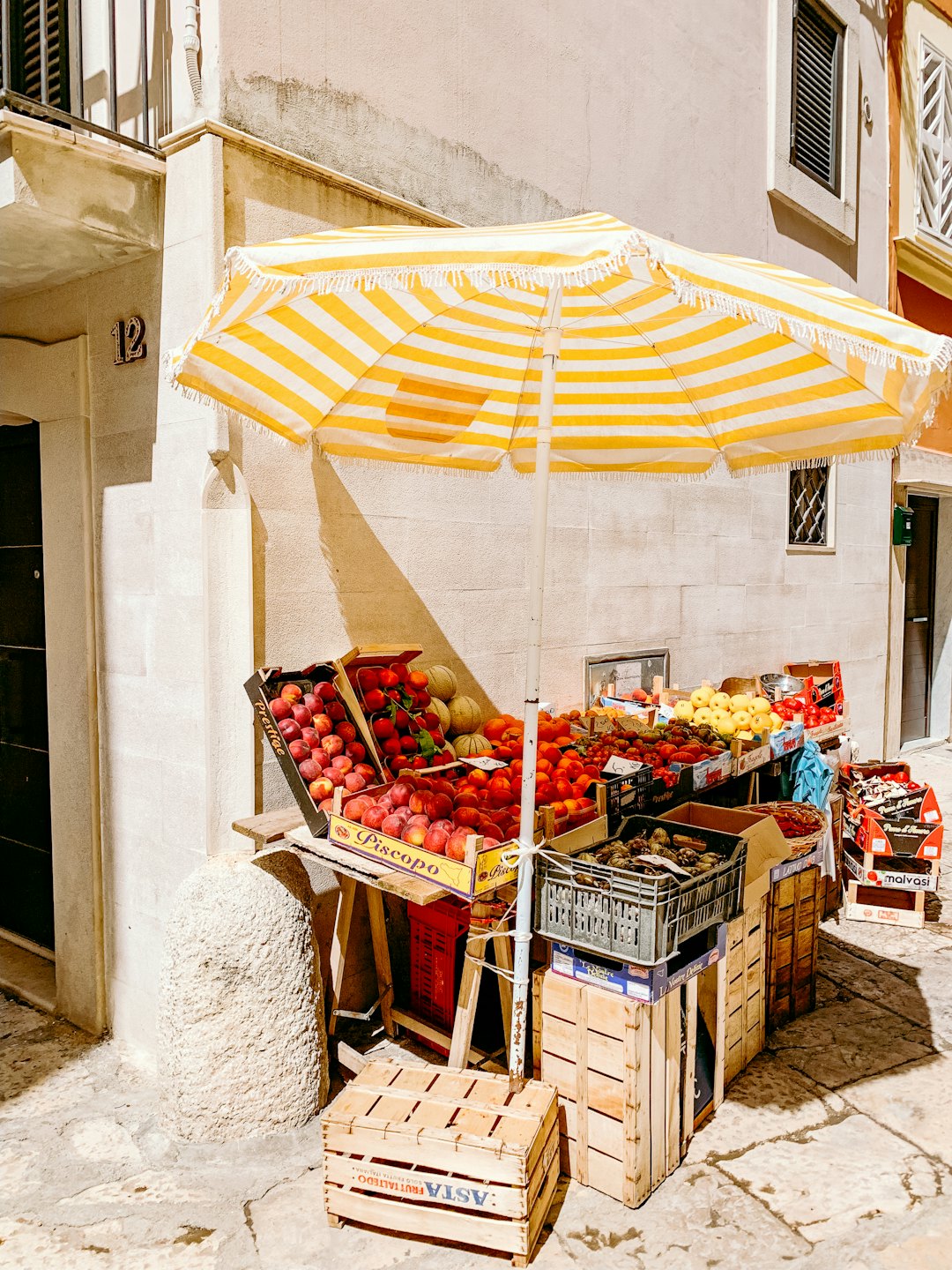 Outdoor market stall with fresh produce under a striped umbrella.